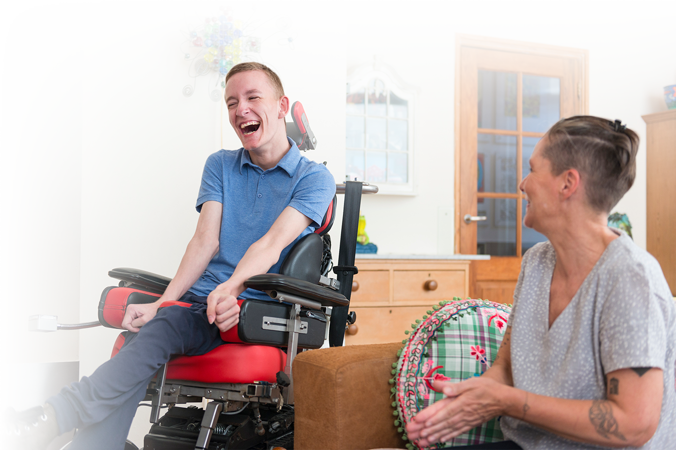 Photo of a young man in a power wheelchair with a female friend as they laugh. Photo of a young man in a power wheelchair with a female friend as they laugh.